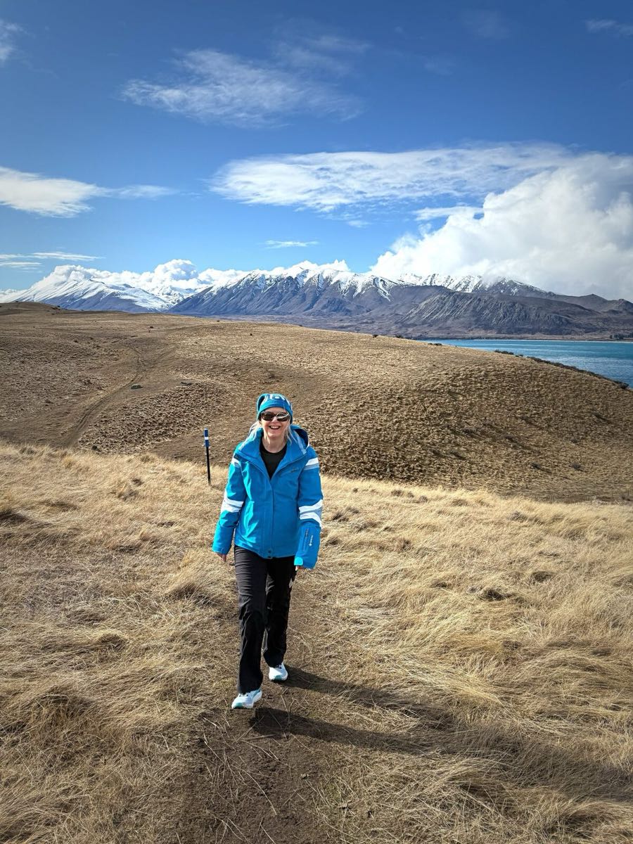 Michelle walking in the high country with snow-capped mountains and a blue lake behind her